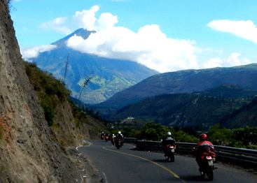 motorcycle tour group riding towards an erupting volcano in ecuador