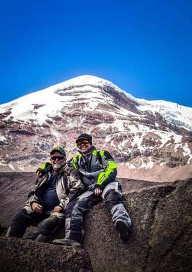 two adventure motorcyclists resting from an adventure motorcycle tour with chimborazo mountain in the background